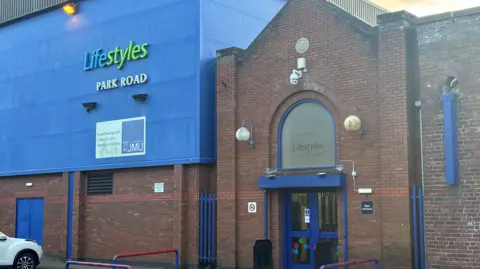 Claire Hamilton/BBC A large brick building connected to a blue warehouse style leisure centre, fitted with a sign reading Lifestyle Park Road in blue, green and white lettering. 