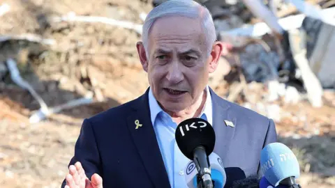 Benjamin Netanyahu gives a statement during a visit to the site of the Weizmann Institute of Science, which was hit by an Iranian missile barrage. He wears a light blue shirt and navy blazer. 
