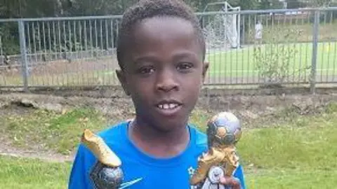 Othniel Adoma wearing football kit and holding two trophies.