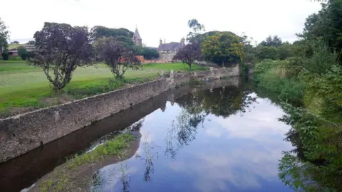 Richard Webb A river with a wall along the side of it and trees reflected