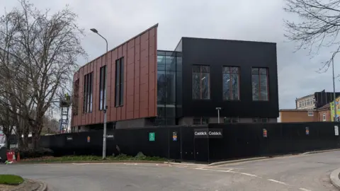 A view on the youth zone. The building is black on one side and brown on the other. A black fence surrounds the site.