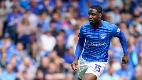 Christian Saydee in action for Portsmouth FC. He is wearing a blue football shirt and white shorts. 