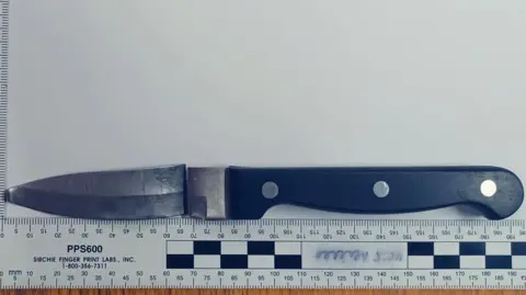 Crown Prosecution Service/Northumbria Police A black handled kitchen knife, the blade has been snapped away from the hilt but that pieced is placed above it in the police photograph. Below is a ruler measuring the blade and handle to be 195cm long