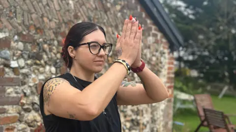 Anna Louise Claydon Ms Corr stands outside in a green garden, one of the outdoor spaces that will be used for warrior movement classes in the warmer weather