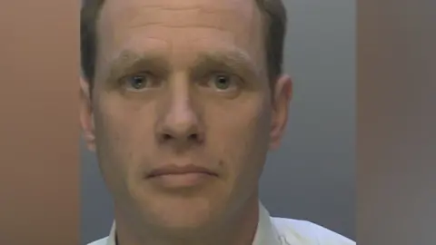 A mugshot of Joel Hanby issued by police. He is wearing a white shirt and looking at the camera.