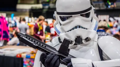 A person dressed as a stormtrooper standing in front of a crowd of people milling around stalls