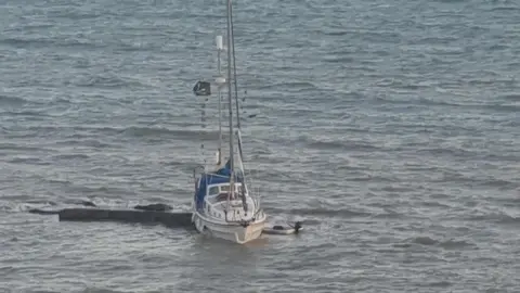 Sarah Baldwin A small white boat run aground on rocks. 