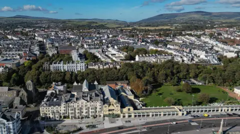Douglas promenade and inland rooftops from the air on a sunny day with the rolling green hills in the background.