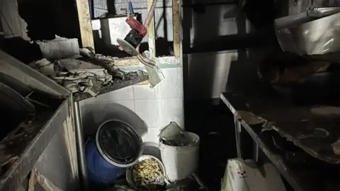 A chip shop that has been devastated in a fire. Rubble can be seen on the floor of the shop, while cabinets and the walls have been burned.