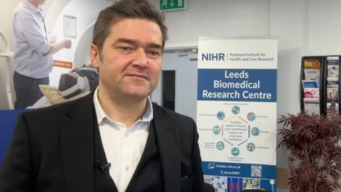 Abi Jaiyeola/BBC Prof Sinisa Savic, a man with dark hair wearing a suit in the Leeds Biomedical Research Centre