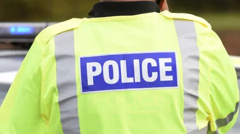 The back and shoulders of a police officer in a hi-vis police jacket.