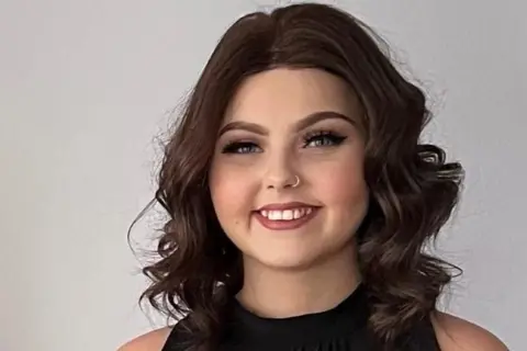 Molly Cuddihy, a young woman with curly long dark hair and a black sleeveless top, smiles broadly at the camera. 