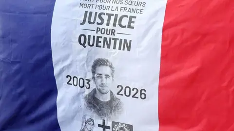 French flag fills the picture. In the centre (on the white stripe of the flag) is a picture of Quentin Deranque with the years 2003 and 2026, and the words in French: "Justice for Quentin".