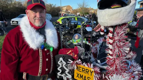 BBC Mark Spindley is the ride organiser, he's dressed as Father Christmas and his bike has red and white tinsel on it with a Merry Xmas number plate
