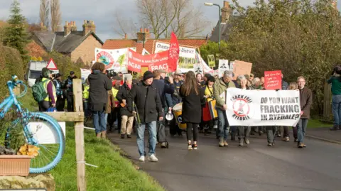 Group of people carrying banners along a road to protest against fracking