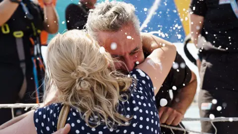 Laura Jackson A man and a woman, wearing a navy dress with white spots, embrace. Confetti can be seen all around them.