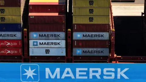 Containers, some of them reading "Maersk", on board a giant cargo ship, again with the Maersk logo.