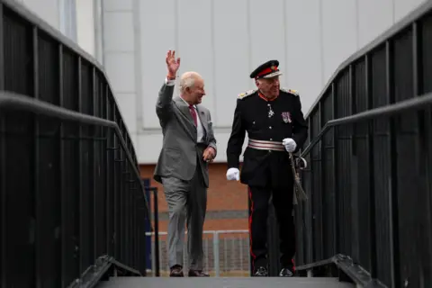 Reuters King Charles waves to people gathered near the Horizon Youth Zone in Grimsby. He is dressed in a grey suit.