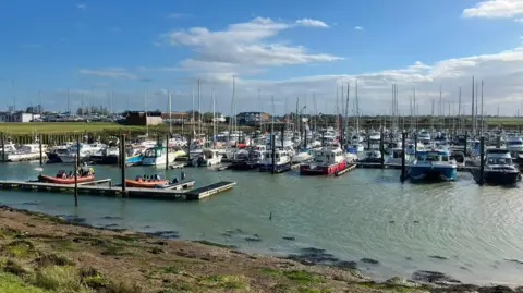 Joshua-Homes Bright/BBC Dozens of boats docked at a marina on an a sunny day. 