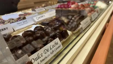 George Carden/BBC Rows of chocolate behind a glass cabinet, the nearest one says dulce de leche which is a south american soft caramel 