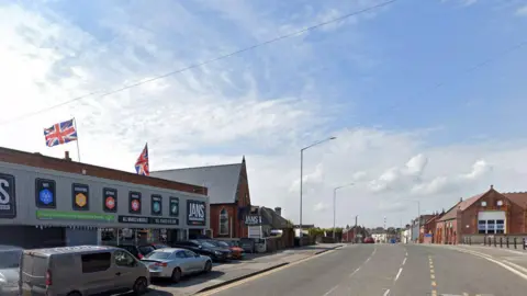 Google Streetview image of Mansfield Road, Sutton in Ashfield, showing a industrial unit with cars outside and, a short distance further along, a red brick primary school building.