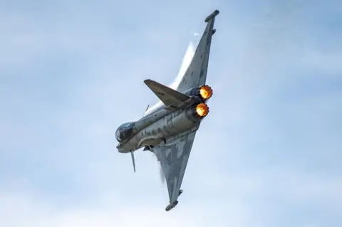 A Eurofighter jet makes a tight mid-air turn showing its engine afterburners glowing bright orange.