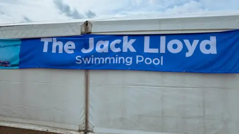 Hampton Vale Primary School The side of a white marquee with a blue sign that reads: "The Jack Lloyd Swimming Pool". 