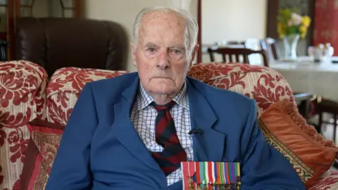 Max looking into the camera and wearing war medals and a tie and jacket.