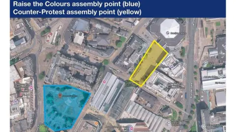 Google/South Yorkshire Police A detailed aerial map of part of a city centre with a blue title banner at the top. The banner contains the text: “Raise the Colours assembly point (blue) Counter-Protest assembly point (yellow)”. The map beneath the title highlights two distinct areas using coloured overlays. On the left side, a blue shaded area marks the assembly point for the “Raise the Colours” group. This blue area surrounds a circular space labelled “Peace Gardens”, which is near Sheffield Town Hall. The blue boundary neatly encloses paths, fountains, and open pedestrian space within the gardens. On the right side of the map, a yellow shaded area indicates the counter-protest assembly point. This yellow shape is long and rectangular in form and stretches along a section near “Tudor Square”. It is positioned close to buildings such as the Lyceum Theatre, the Crucible Theatre, and the Winter Garden. The yellow zone appears to follow a walkway or plaza area between these structures.
