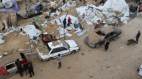 Reuters are three vehicles buried in sand after strike, and several tents and people's belongings