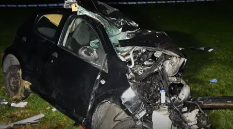 BBC Crimewatch Live Wreckage of the dark-coloured Citroen C1 in the aftermath of the crash. The wheels are misaligned, causing the roof and front of the vehicle to be crumpled by the impact