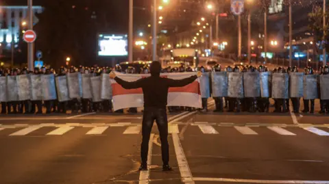 Badan Pressphoto Eropa Sebuah protes adalah Belarus, Agustus 2020. Seorang pria yang sendirian memegang bendera putih dengan garis merah hingga kerumunan polisi anti huru hara. 