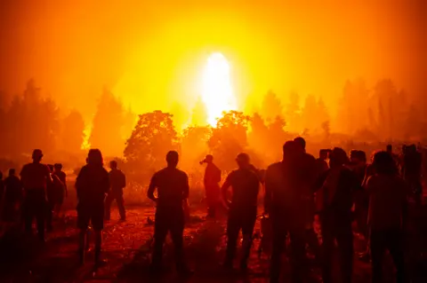 ANGELOS TZORTZINIS / AFP Local volunteers gather in an open field and wait to support fire fighters during a wildfire next to the village of Kamatriades, Evia island, Greece