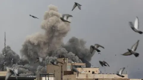 An explosion from a building in Tehran as birds fly away.