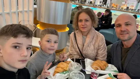 Mum and dad sat with their two boys at a restaurant with croissants.