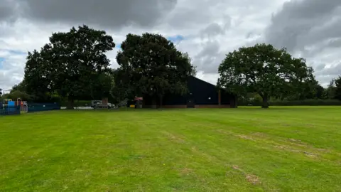 Jodie Halford/BBC Three oak trees stand in a field next to a village hall