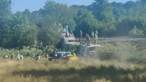 People standing on a train that is on its side.
