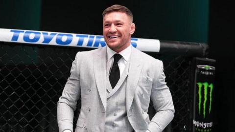 Conor McGregor smiles in the octagon in a grey suit