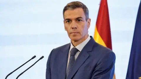 Pedro Sanchez, who has a neutral expression and short greying brown hair, wears a suit and tie as he listens during a press conference