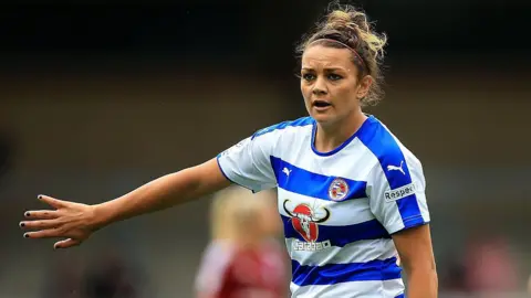 Getty Images Nia Jones playing football for Reading FC Women in 2016. She has a stern expression and holds her right arm up in the air. 