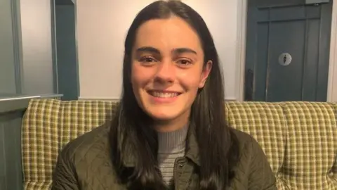 Family handout is white, white hair is white and smile on camera. He has brown eyes and is wearing an olive colored jacket.