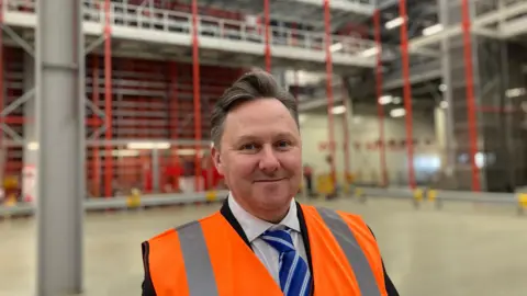 Andrew Baxter in a shirt and tie and hi-vis vest in a wharehouse.