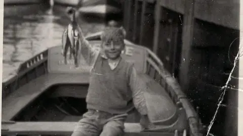 Fred Normandale A black and white photograph of a little boy sitting in a fishing boat holding up whiting.