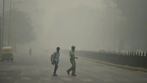 AFP Two pedestrians on road in New Delhi engulfed in smog from last year