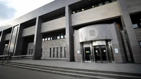 The exterior of Glasgow Sheriff Court, a grey building with a rotating door entrance