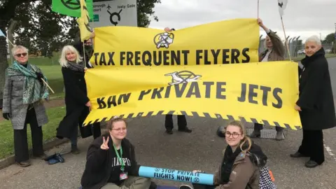 XR South East UK XR protesters with signs saying 'tax frequent flyers' and 'ban private jets'