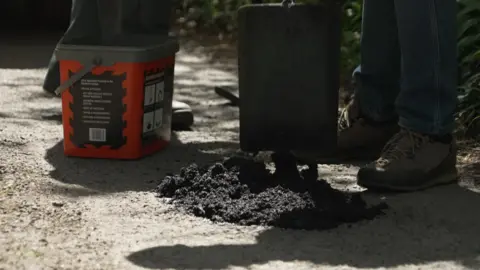 A volunteer laying down product to fix a pothole with a spade.
