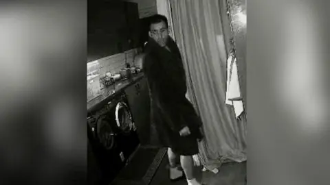 Gloucestershire Constabulary A black and white CCTV photo of James Brown in someone's kitchen wearing a dressing gown and sliders.