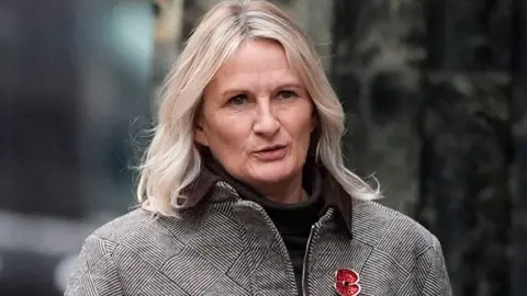 PA Media Lucy Ward with blond bobbed hair arrives at Liverpool Crown Court wearing a dog tooth patterned jacket and black roll neck jumper.