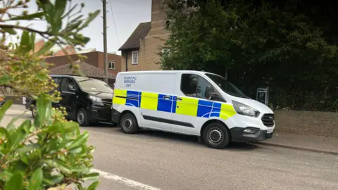 Emma Baugh/BBC Image shows two vans, one of them a police van with "scientific services unit" written on the site.